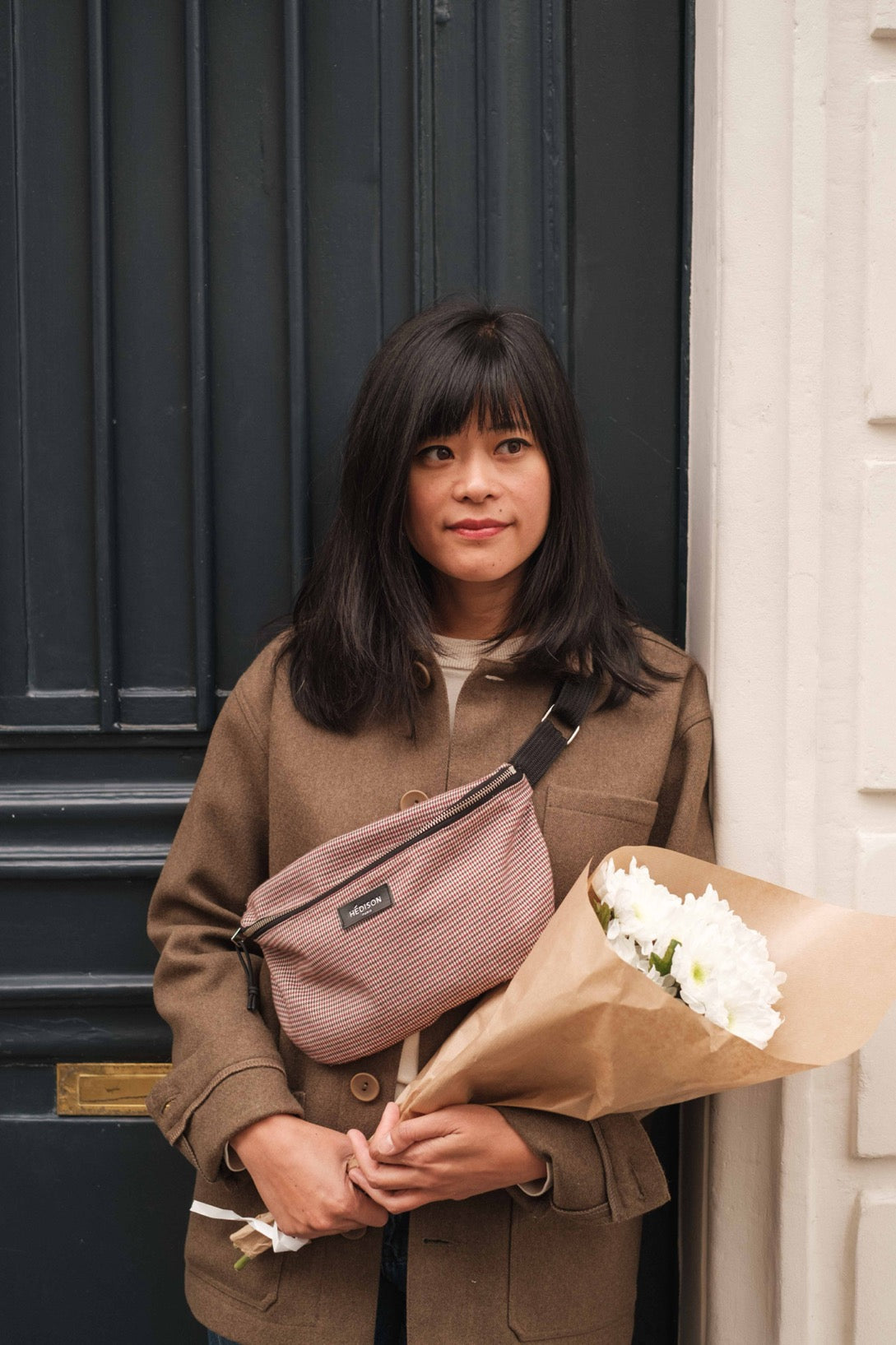 Une femme tenant un bouquet de fleurs et portant un sac banane en bandoulière Hédison Paris